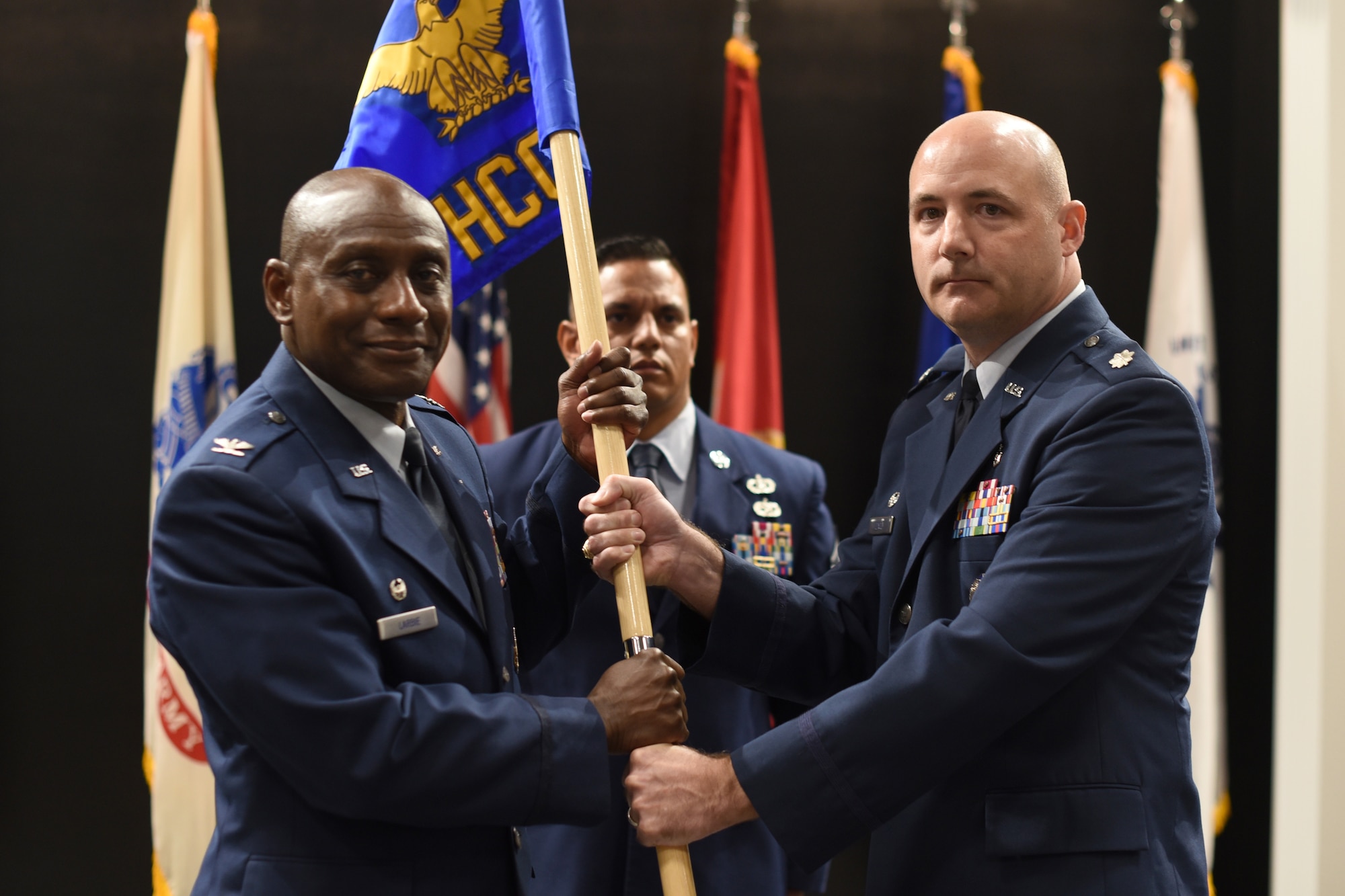 U.S. Air Force Lt. Col. Danny Dacey, right, 17th Healthcare Operations Squadron outgoing commander, relinquishes command to Col. Derek Larbie, 17th Medical Group commander, during the 17th HCOS change of command ceremony at the Powell Event Center, Goodfellow Air Force Base, Texas, June 10, 2022. Passing the guidon physically represents the symbolism of passing the squadron responsibilities to the next commander. (U.S. Air Force photo by Senior Airman Abbey Rieves)