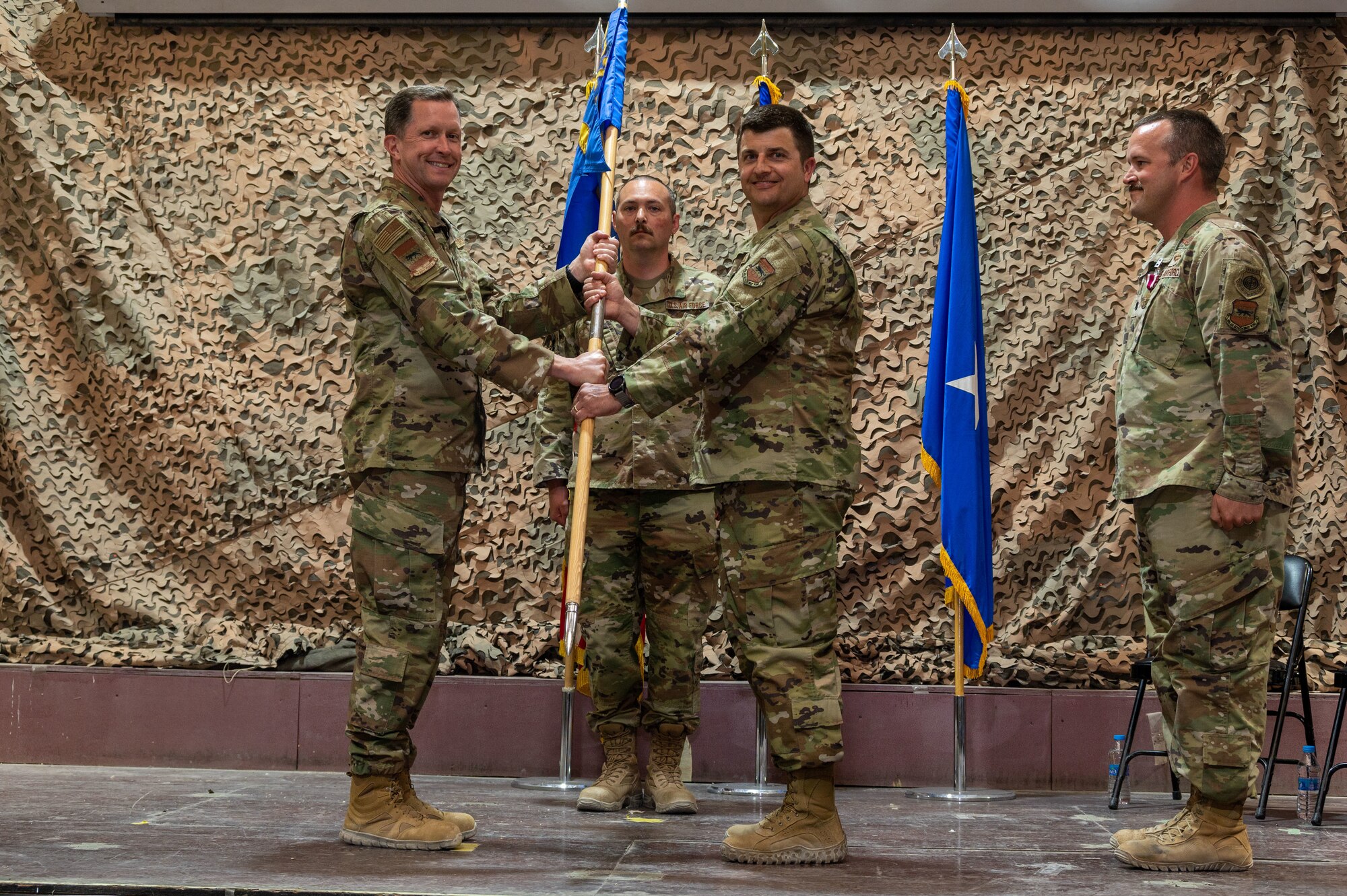 U.S. Air Force Brig. Gen. Christopher Sage, 332d Air Expeditionary Wing commander, exchanges the 332d Expeditionary Operations Support Squadron guidon with U.S. Air Force Lt. Col. James A. Harris, 332d OSS incoming commander, during a change of command ceremony at an undisclosed location in Southwest Asia, June 4, 2022. A change of command ceremony is a tradition that represents a formal transfer of authority and responsibility from the outgoing commander to the incoming commander. (U.S. Air Force photo by Tech. Sgt. Lauren M. Snyder)