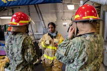 Damage Controlman 3rd Class Kyla Embry, assigned to the Zumwalt-class destroyer USS Michael Monsoor (DDG 1001), teaches U.S. Naval Sea Cadets how to properly wear a firefighter's helmet aboard the ship during Portland Fleet Week 2022.