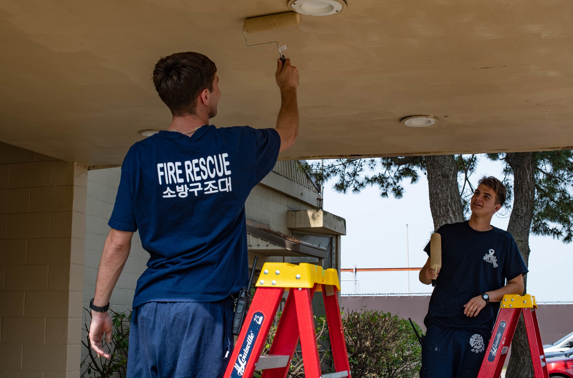 Two people apply paint to a roof