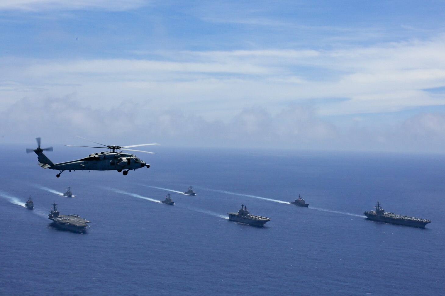 PHILIPPINE SEA (June 12, 2022) An MH-60S Sea Hawk helicopter, assigned to the “Chargers” of Helicopter Sea Combat Squadron (HSC) 14, flies above the Nimitz-class aircraft carrier USS Abraham Lincoln (CVN 72), front left, America-class amphibious assault ship USS Tripoli (LHA 7), front center, Nimitz-class aircraft carrier USS Ronald Reagan (CVN 76), front right, Ticonderoga-class guided-missile cruiser USS Mobile Bay (CG 53), middle left, Arleigh Burke-class guided-missile destroyer USS Benfold (DDG 65), middle center, Ticonderoga-class guided-missile cruiser USS Antietam (CG 54), middle right, Arleigh Burke-class guided-missile destroyer USS Spruance (DDG 111), back left, and Arleigh Burke-class guided-missile destroyer USS Fitzgerald (DDG 62) as they sail in formation during Valiant Shield 2022 (VS22). VS22 is a U.S.-only, biennial field training exercise (FTX) focused on integration of joint training in a multi-domain environment. This training builds real-world proficiency in sustaining joint forces through detecting, locating, tracking, and engaging units at sea, in the air, on land, and in cyberspace in response to a range of mission areas. (U.S. Navy photo by Mass Communication Specialist Seaman Aleksandr Freutel)