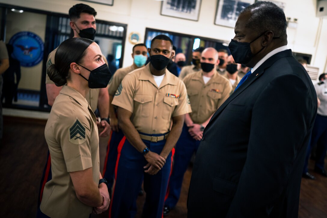 A man in business attire faces a woman in a military uniform. Both are wearing face masks.