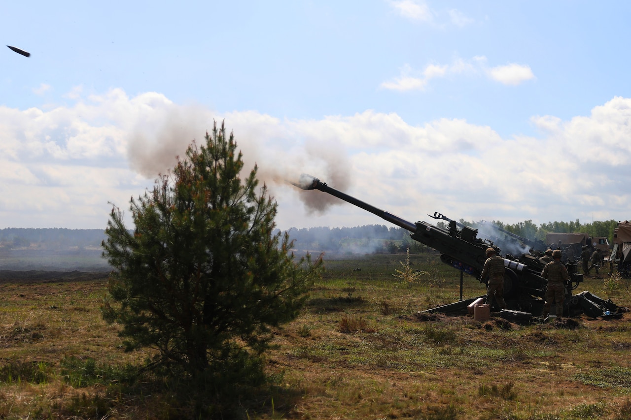 Soldiers fire a large artillery weapon set up in a field.