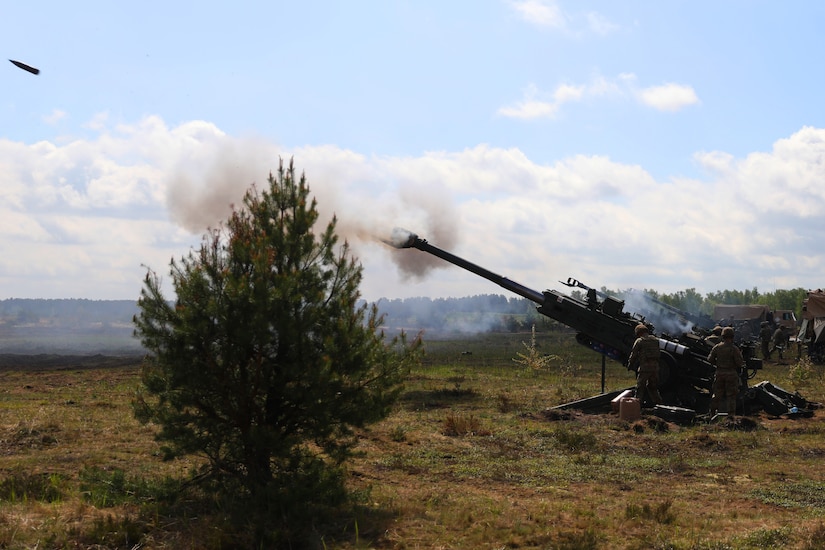 Soldiers fire a large artillery weapon set up in a field.