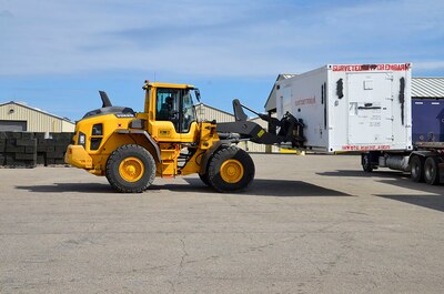 A large piece of yellow Equipment is used to off-load a flat bed semi trailer.