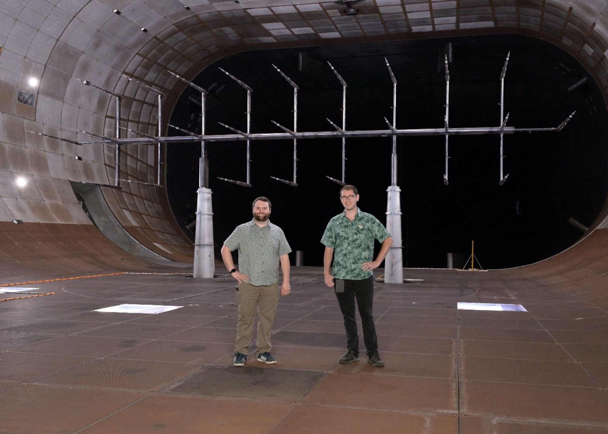 Kyle Lukacovic, a test engineer at the National Full-Scale Aerodynamics Complex (NFAC), left, and Paul Gilles, an NFAC instrumentation engineer, pause for a photo in the 40-foot by 80-foot Wind Tunnel of NFAC at Moffett Field, Calif., where a flow characterization study was recently completed. During the multi-phased effort, updates were made to the existing flow calibration and characterization in the tunnel. Pictured behind Giles and Lukacovic is the test rig used for the flow evaluation. NFAC is an operating location of the 716th Test Squadron, 804th Test Group, Arnold Engineering Development Complex. (U.S. Air Force photo) (This image was altered by obscuring a badge for security purposes)