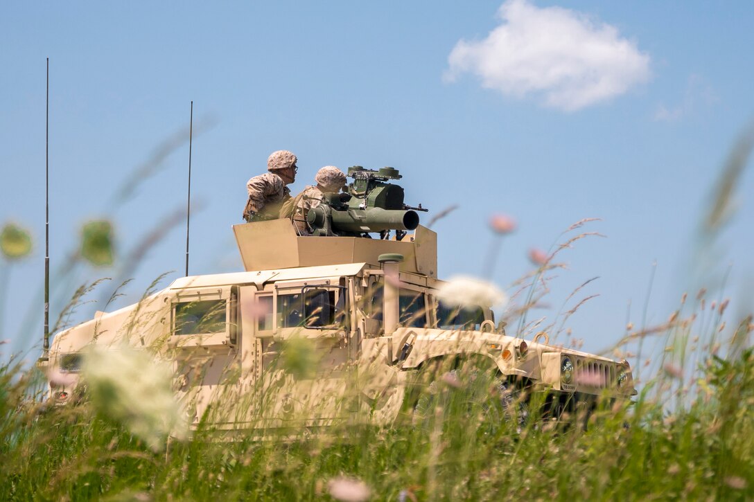 Marines fire from an armored vehicle in a field.