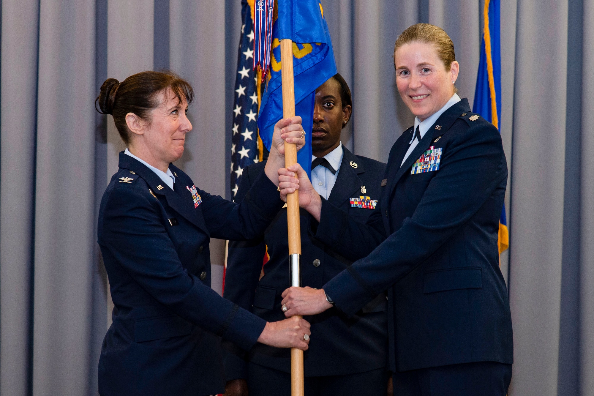 Lt. Col. Brittany Nutt, outgoing 436th Health Care Operations Squadron commander, right, relinquishes command of the 436th HCOS after handing the guidon to Col. Tracy Allen, left, 436th Medical Group commander, during a change of command ceremony held at The Landings on Dover Air Force Base, Delaware, June 9, 2022. The 436th HCOS Change of Command was one of four ceremonies conducted within the 436th MDG. Guidon bearer for the ceremony was Master Sgt. Kimberly Hammonds, center, 436th HCOS superintendent. (U.S. Air Force photo by Roland Balik)