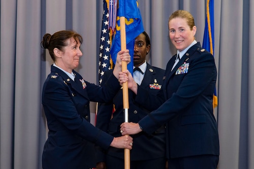 Lt. Col. Brittany Nutt, outgoing 436th Health Care Operations Squadron commander, right, relinquishes command of the 436th HCOS after handing the guidon to Col. Tracy Allen, left, 436th Medical Group commander, during a change of command ceremony held at The Landings on Dover Air Force Base, Delaware, June 9, 2022. The 436th HCOS Change of Command was one of four ceremonies conducted within the 436th MDG. Guidon bearer for the ceremony was Master Sgt. Kimberly Hammonds, center, 436th HCOS superintendent. (U.S. Air Force photo by Roland Balik)