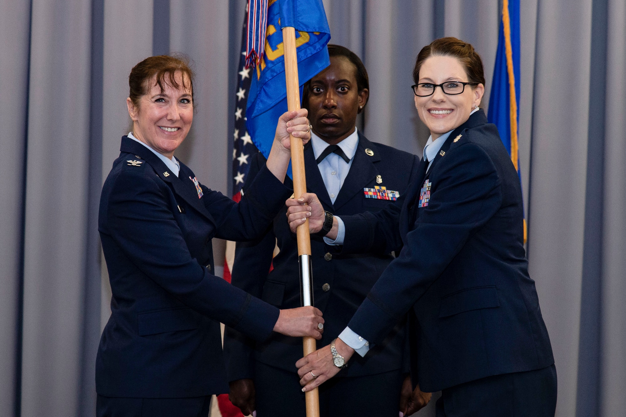 Lt. Col. Sara Spearing, 436th Health Care Operations Squadron commander, right, assumes command of the 436th HCOS after receiving the guidon from Col. Tracy Allen, left, 436th Medical Group commander, during a change of command ceremony held at The Landings on Dover Air Force Base, Delaware, June 9, 2022. The 436th HCOS Change of Command was one of four ceremonies conducted within the 436th MDG. Guidon bearer for the ceremony was Master Sgt. Kimberly Hammonds, center, 436th HCOS superintendent. (U.S. Air Force photo by Roland Balik)