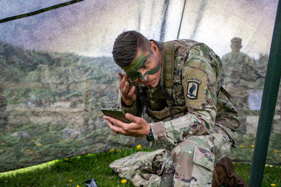 A soldier kneels and applies camouflage paint to his face.