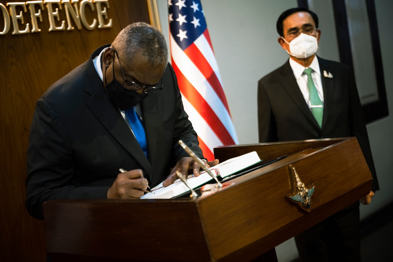 Service members are seated around a table with two men in business attire sitting at its head.