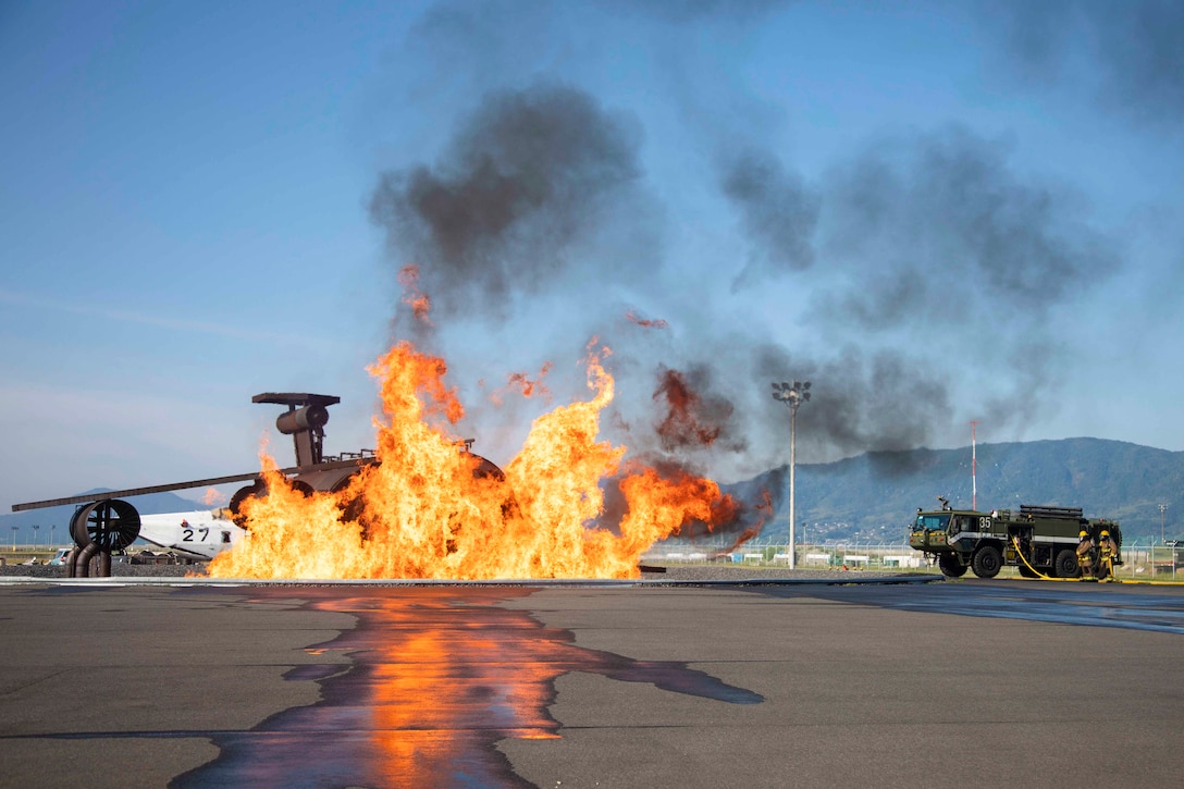 Marines hold a hose next to a truck in front of an aircraft fire.