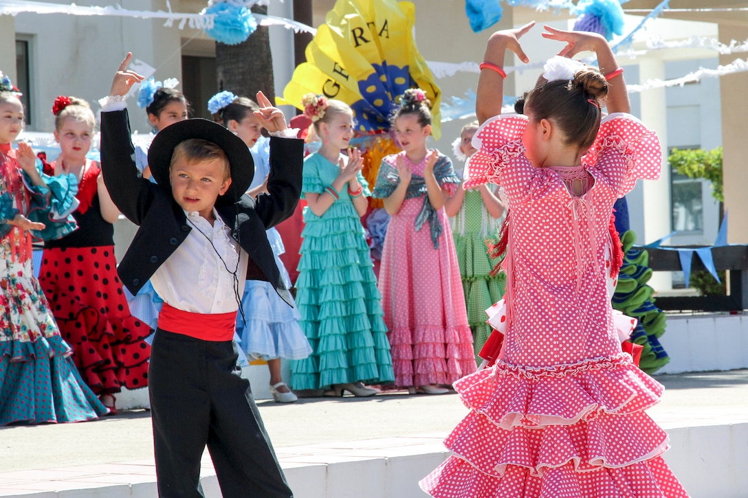 Children in traditional Spanish garb dance as others watch.