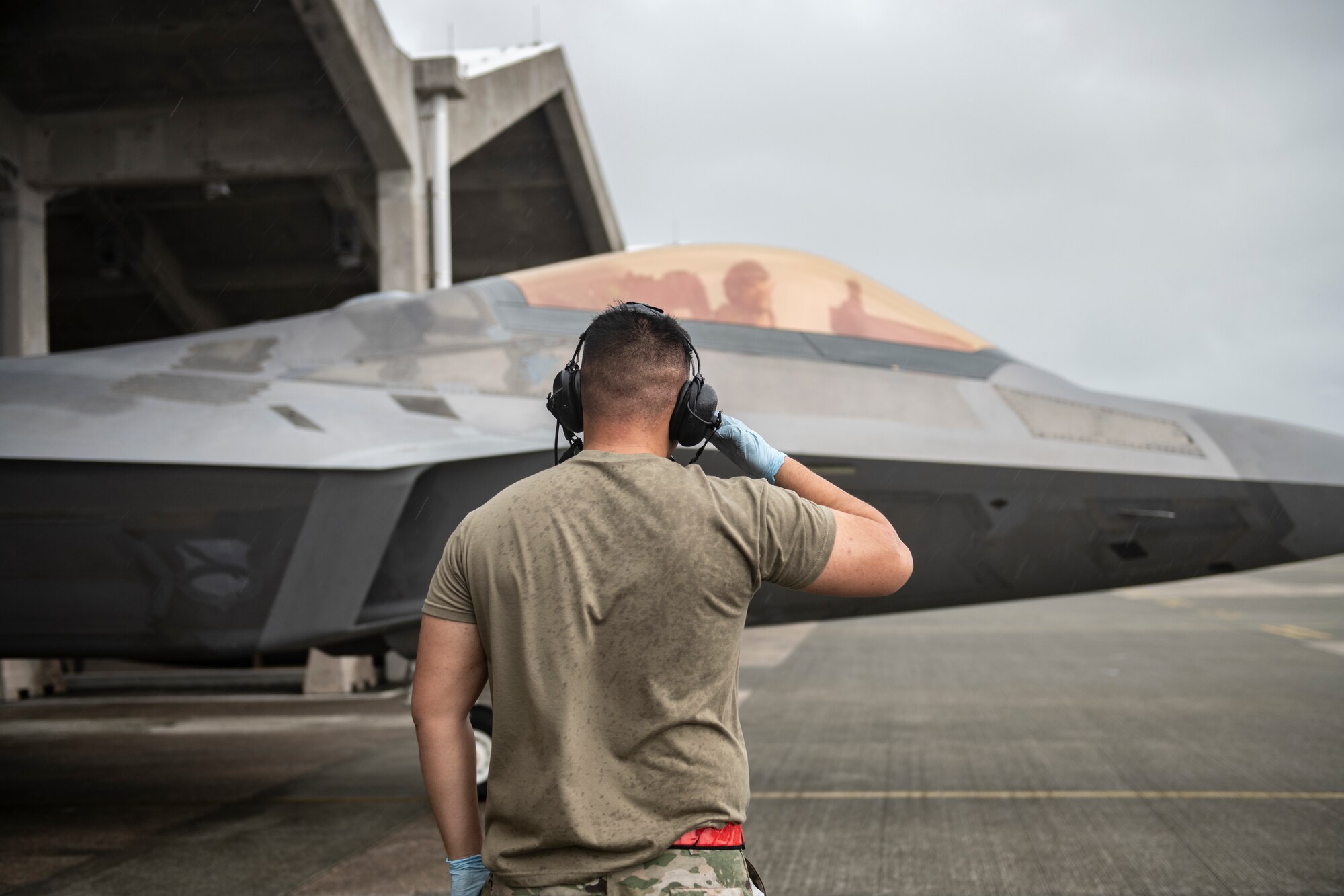 Photo of a crew chief marshalling an F-22 out of a hangar