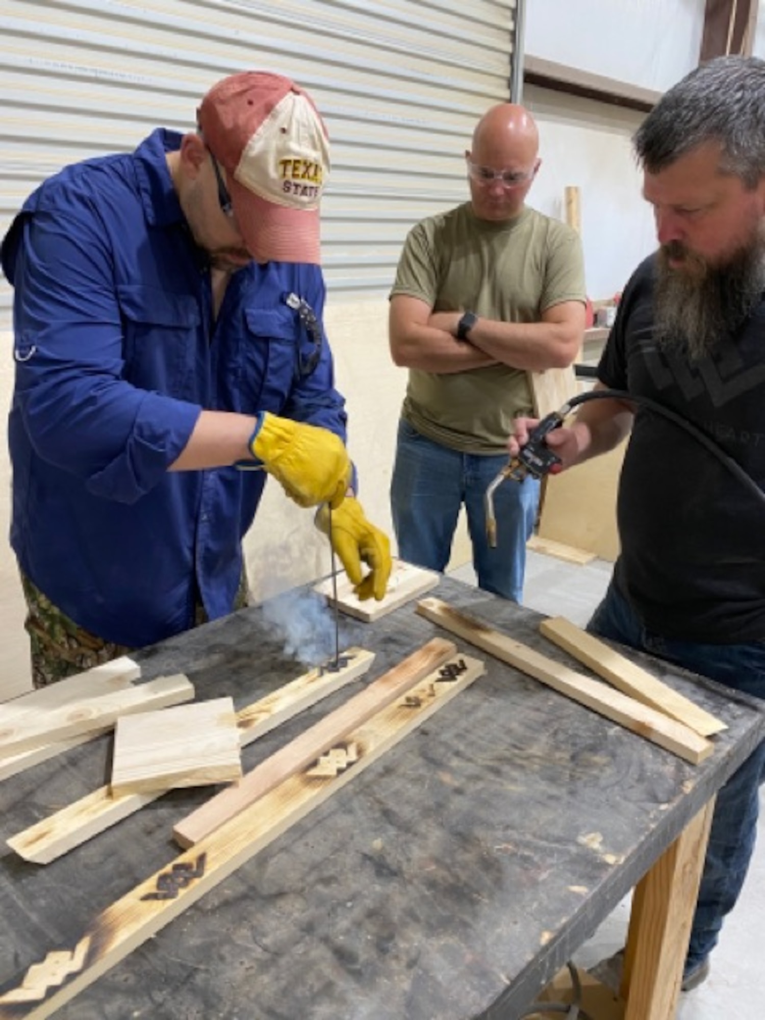 Justin Jordan, Warriors Heart director of business development (right), coaches Bud Boehnke, 960th Cyberspace Wing process manager (left), and Senior Master Sgt. Ryan Dirnberg, 960th Cyberspace Operations Group standardization and evaluation superintendent, as they learn how to burn decorations into wood May 31, 2022, at the Warriors Heart Treatment Center in Bandera, Texas