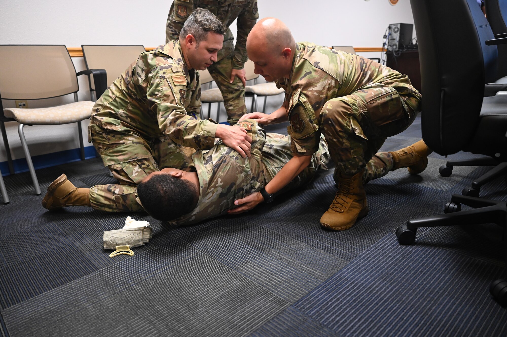 Senior Airman Cesar Zayas, 960th Cyberspace Operations Group client support technician, and Tech. Sgt. Jesse Richter, 960th Operations Support Flight current operations NCOIC, prepare to roll Staff Sgt. Kendall Armand, 960th COG client support technician, to the recovery position during a tactical combat casualty care training class June 4, 2022, at Joint Base San Antonio-Chapman Training Annex, Texas.