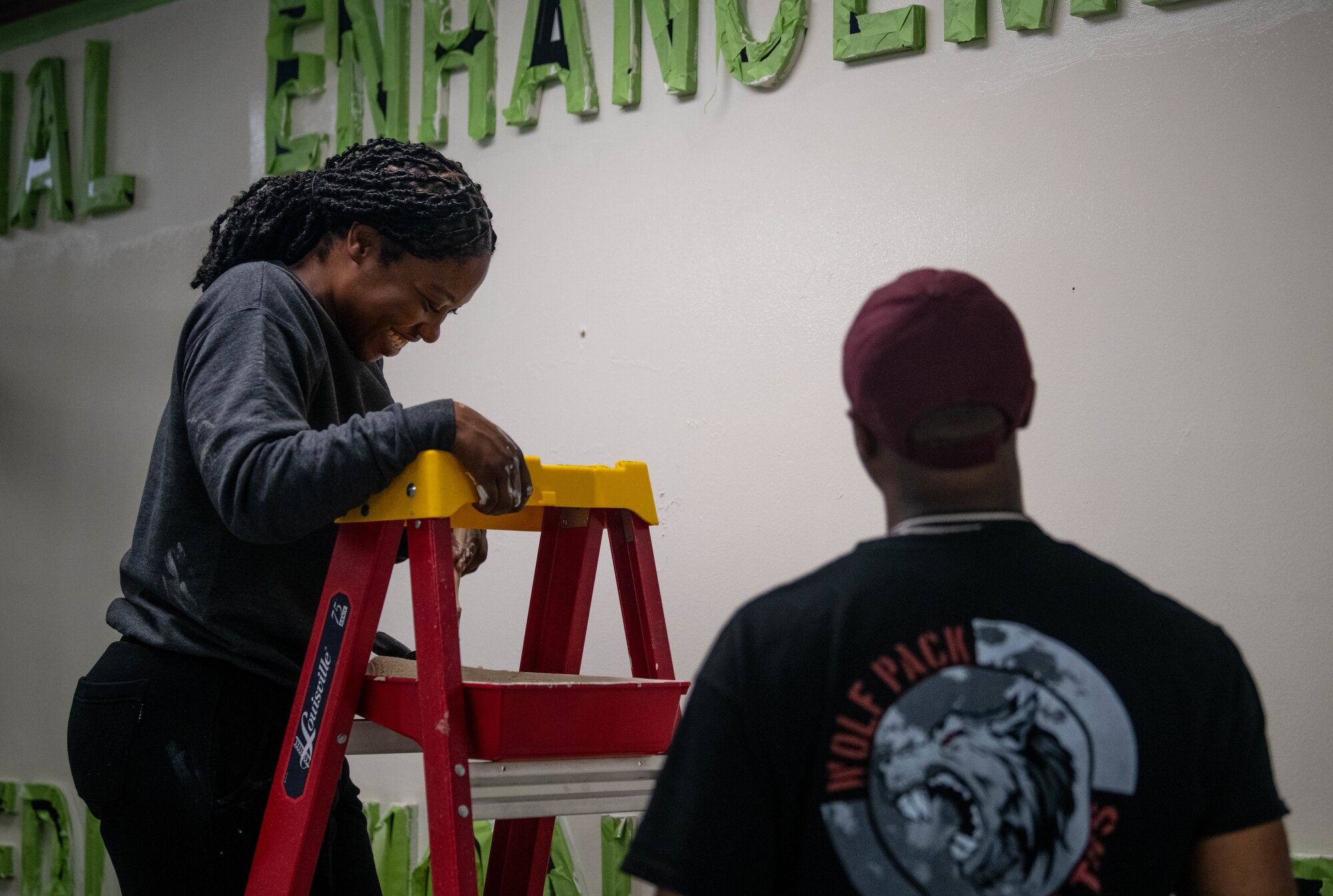 Two people talk while on a ladder, painting