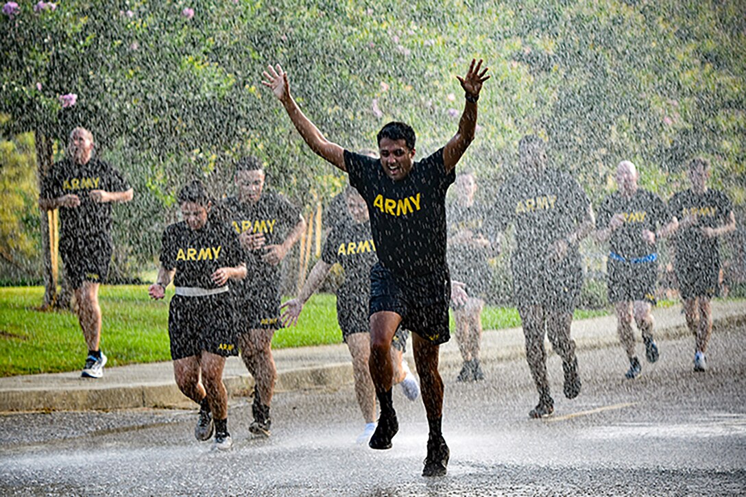 Soldiers in black Army t-shirts and shorts run on a road through the rain.