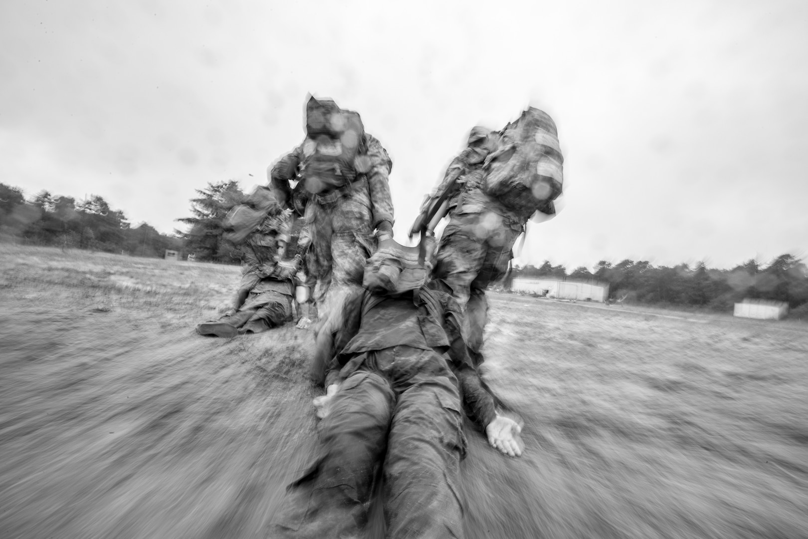 Two teams of two uniformed service members move through a field, with each team pulling a training mannequin across the ground in a field.
