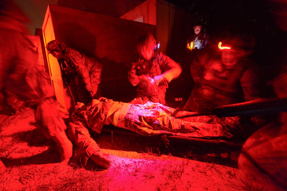 Uniformed service members tend to a service member on a stretcher under a red light at night