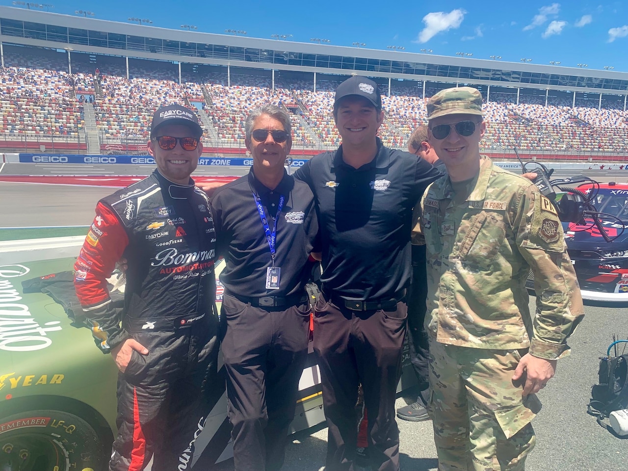 Four men pose in front of a racecar.