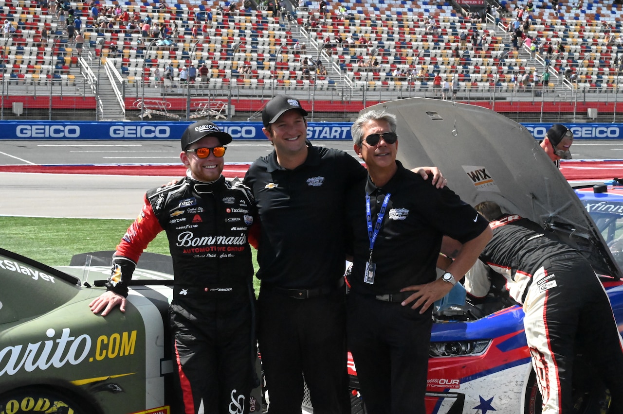 Three men pose in front of a racecar.
