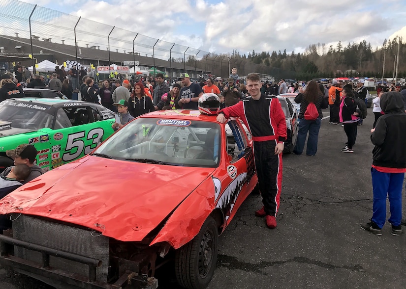 A man poses beside a beat-up racecar.