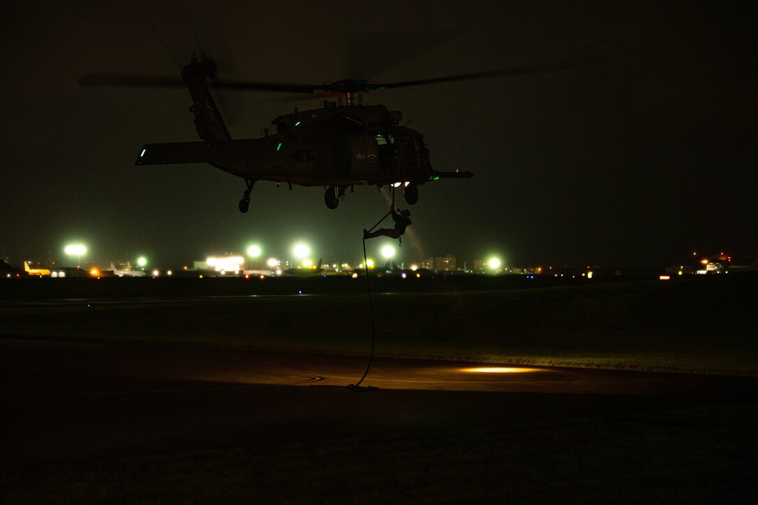 An airman fast-ropes out of an airborne helicopter in the dark.