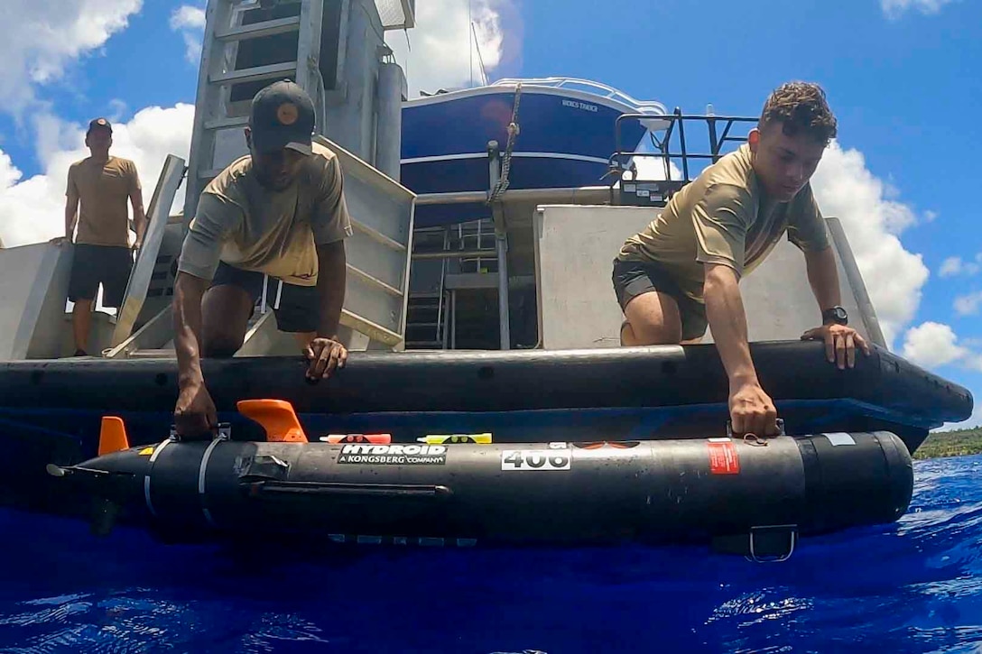 Sailors hold an unmanned underwater vehicle above water.