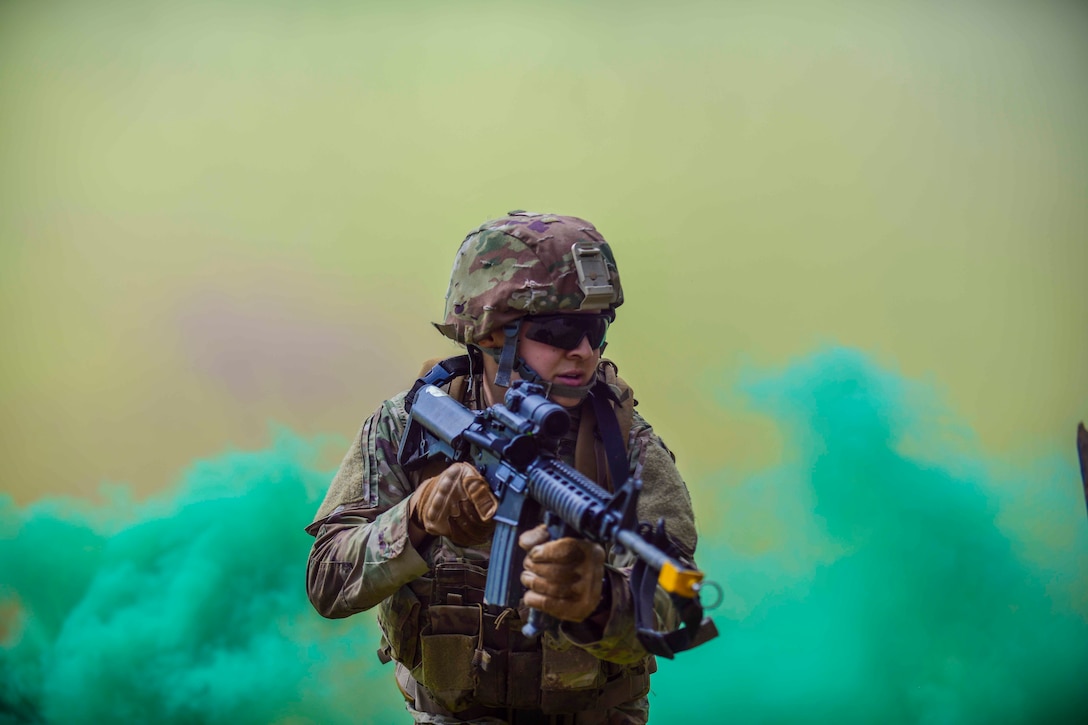 An airman holds a weapon as green smoke rises behind.
