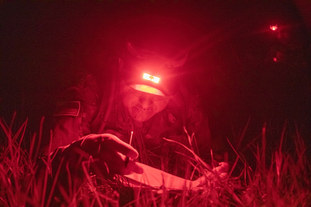 A soldier uses a headlamp to check a map  at night.