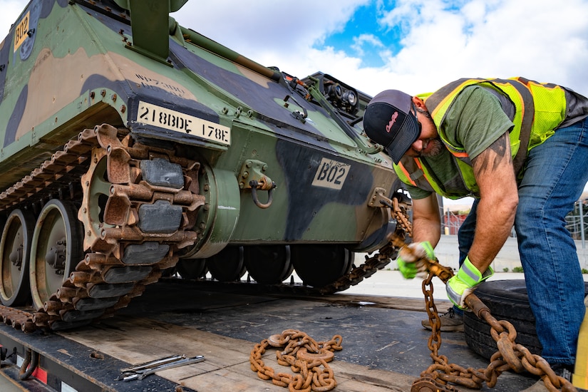 A civilian truck driver secures a military vehicle.