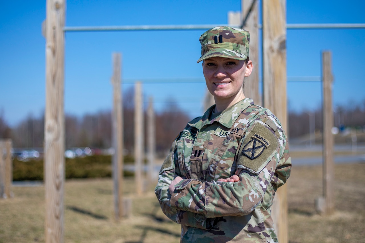 A woman with her arms crossed stands near pullup bars smiles for a photo.