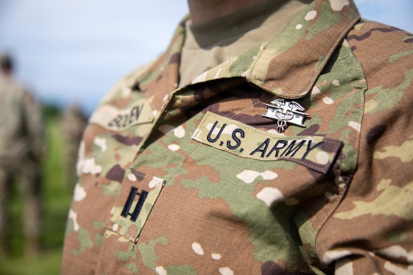 A silver medical badge is pinned onto the chest of a uniform above a “U.S. Army” branch tape.