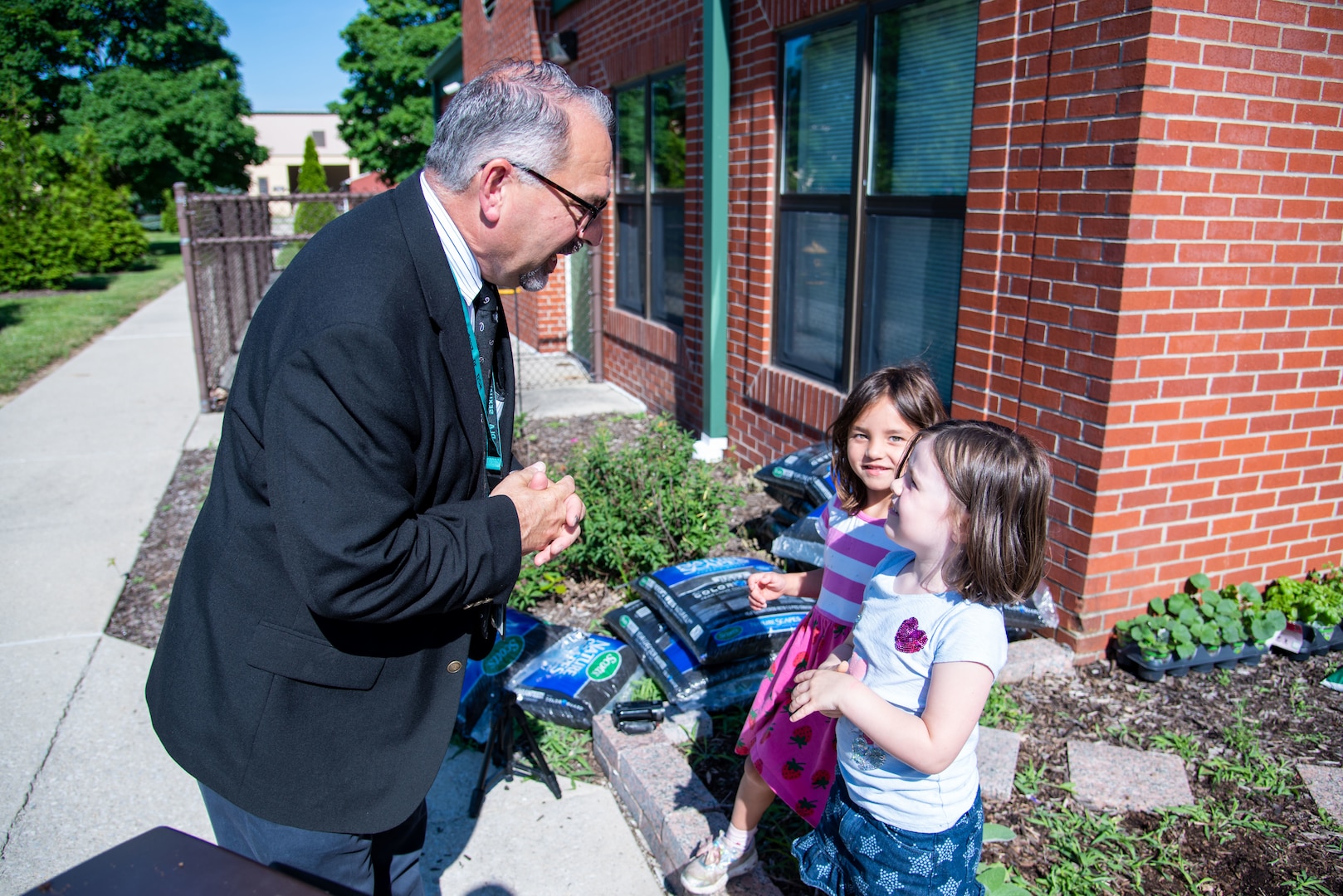A man in a business suit talks with two children after they planted plants at the CDC garden.
