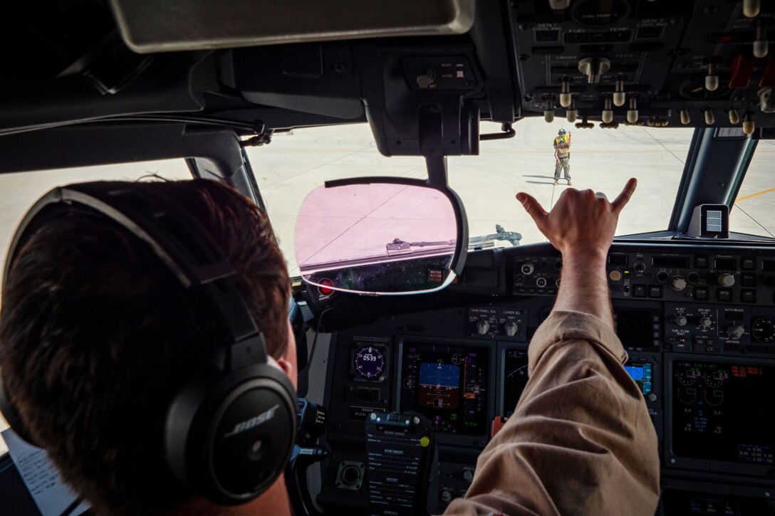 A pilot in a cockpit signals to someone on the ground.