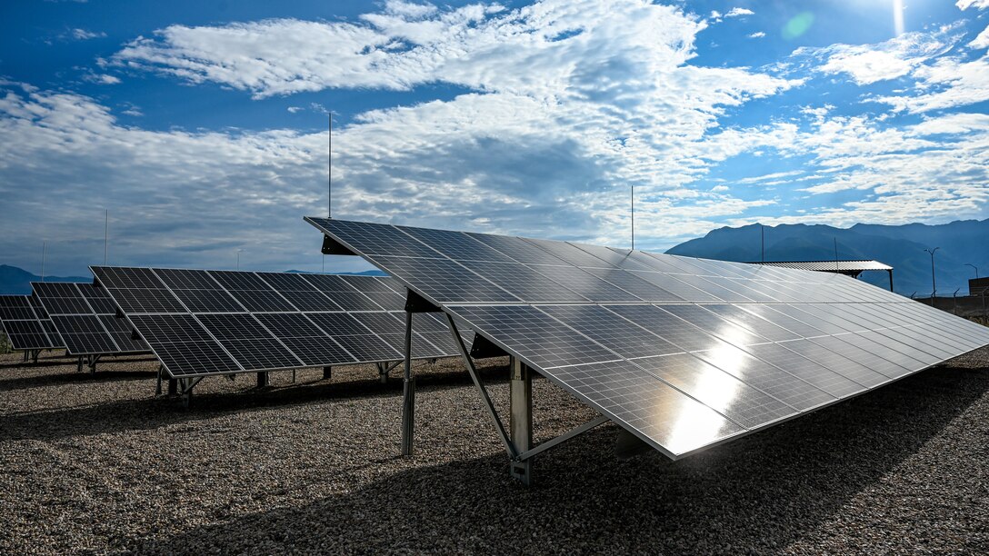 A line of solar panels reflect the sun on a partly cloudy day.