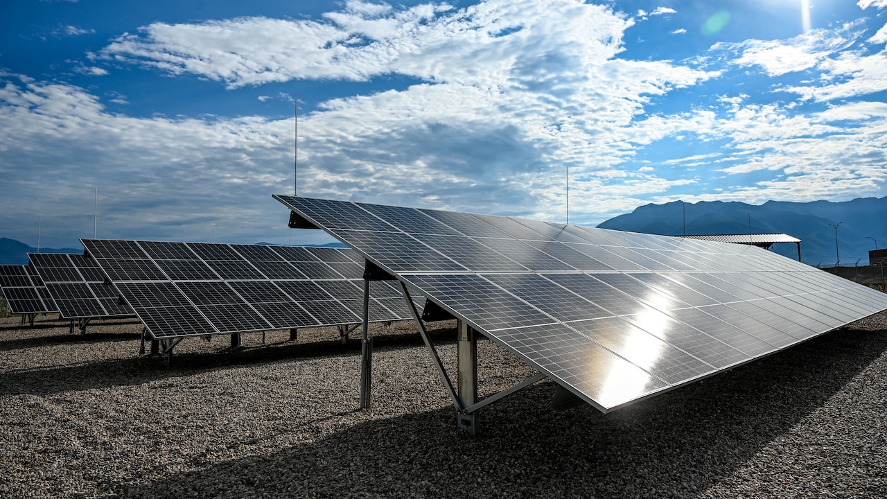 A line of solar panels reflect the sun on a partly cloudy day.