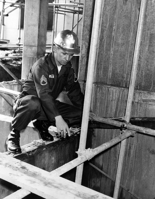 Man in hard hat looks at girders on construction site.