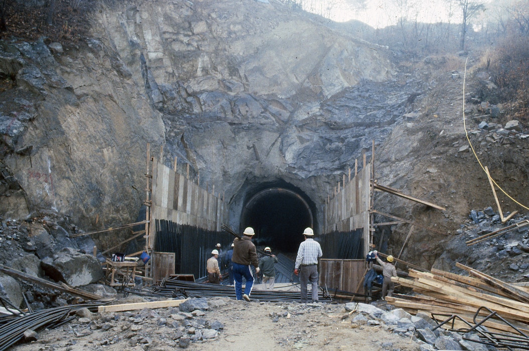 Men stand in front of a tunnel opening in a rock hill.
