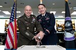 Group photo of many people standing in front of table with cake smiling