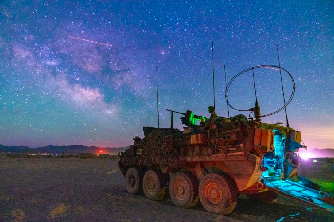 A soldier mans a gun on top of a military vehicle at night.