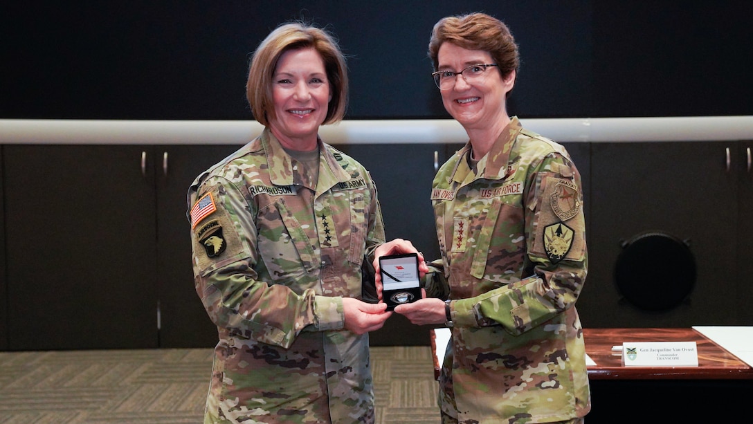 Army Gen. Laura Richardson presents a command coin to Air Force Gen. Jacqueline Van Ovost.