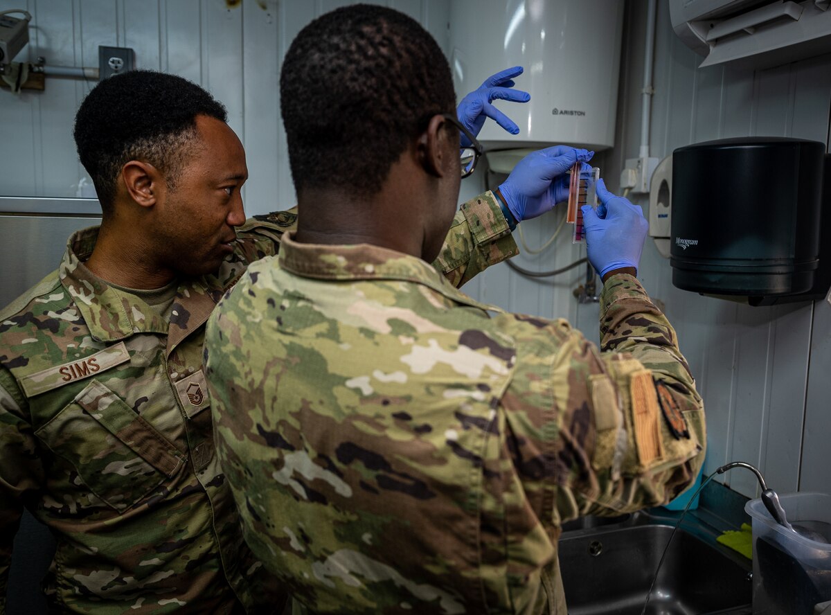 Master Sgt. Justin Sims, Expeditionary Medical Group bioenvironmental engineering craftsman, oversees Senior Airman Kevin Thompson, 332d Expeditionary Civil Engineer Squadron force protection and public health journeyman, taking a water sample at an on-base coffee shop to test for acceptable ranges in pH and chlorine at an undisclosed location in Southwest Asia, May 11, 2022. (U.S. Air Force photo by Master Sgt. Christopher Parr)