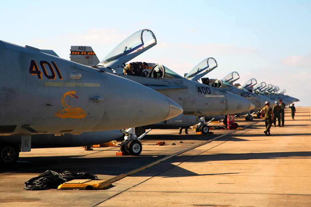 Marines walk down a flight line near a line of parked jets.