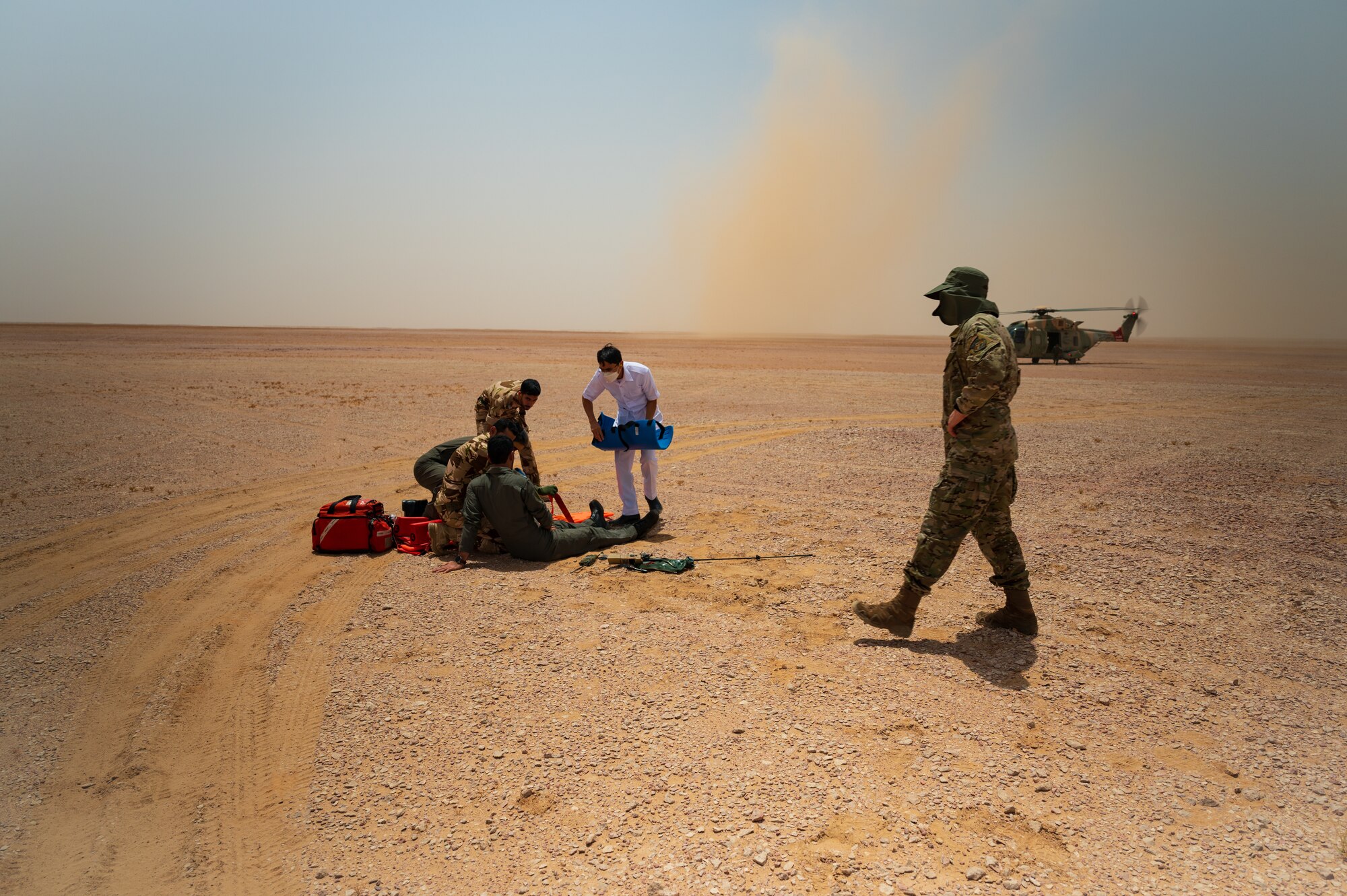 A Royal Air Force of Oman pilot receives simulated medical care in the Oman desert prior to being moved to a waiting rescue helicopter as part of a survival training exercise conducted with U.S. Air Force Tech. Sgt. David Jones, a survival evasion resistance and escape instructor from Air Force Central Command, A3, during Accurate Test 22, May 17, 2022. Jones looked on as simulated medical care was provided and the helicopter remained ready to airlift the pilot and rescue crew away. (U.S. Air Force photo by Staff Sgt. Dana Tourtellotte)