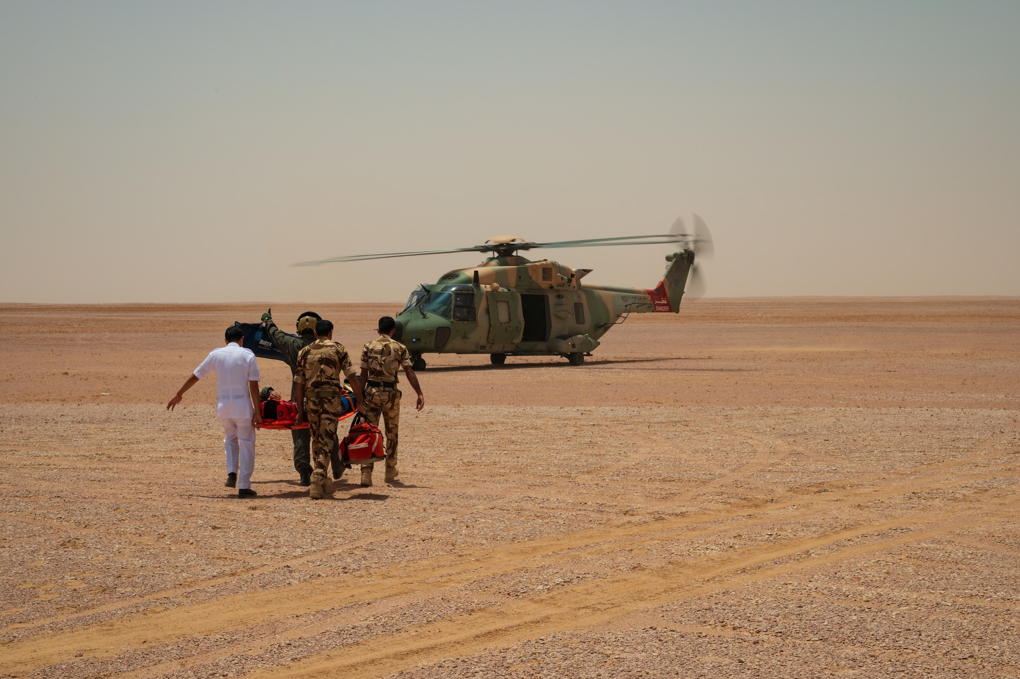 Members of the Royal Air Force of Oman carry a pilot across the open desert in Oman while simulating combat search and rescue operations during Accurate Test 22, May 17, 2022. The RAFO crew signaled the waiting helicopter pilot on their way back to the aircraft. (U.S. Air Force photo by Staff Sgt. Dana Tourtellotte)
