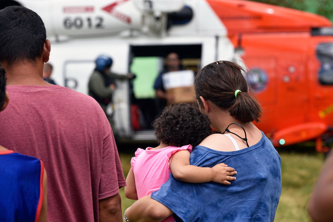 Locals watch as a Coast Guard MH-65 Jayhawk helicopter crew unloads relief supplies in Maricao, Puerto Rico on Oct. 7, 2017. The Coast Guard is helping deliver relief supplies to victims of Hurricane Maria stranded in remote areas by mudslides and washed out roads. (U.S. Coast Guard photo by Petty Officer 3rd Class Eric D. Woodall)