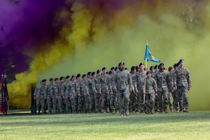A large group of soldiers walk on a field surrounded by yellow and purple smoke.